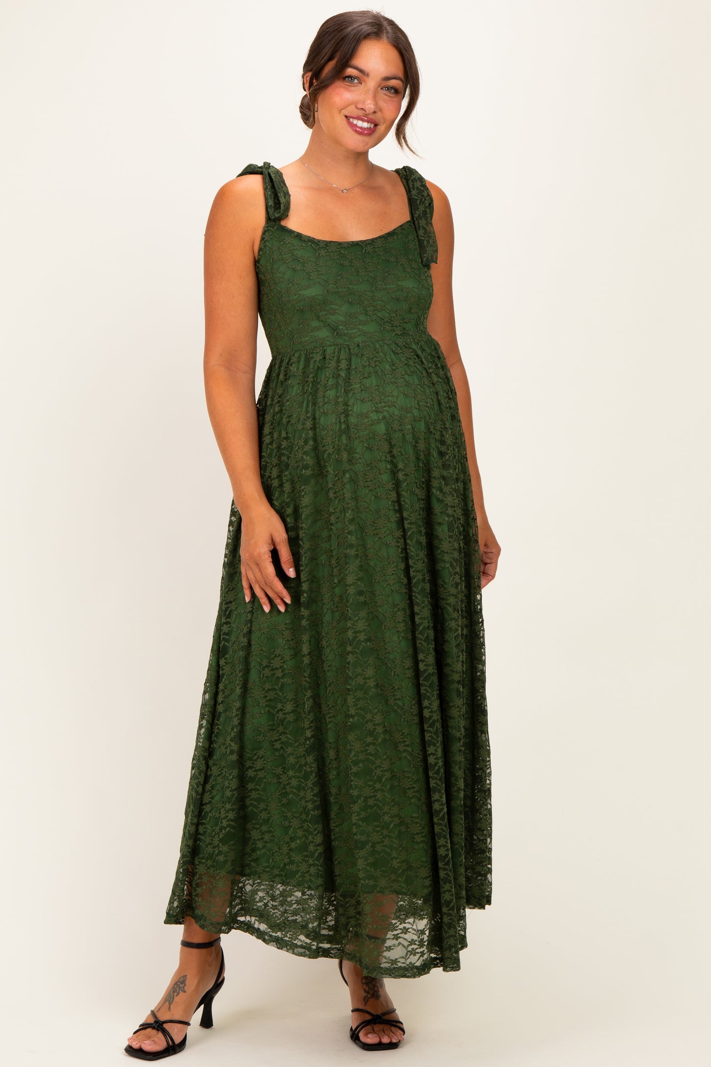 woman wearing a dark green lace maternity maxi dress with bow details on the straps and a visible baby bump