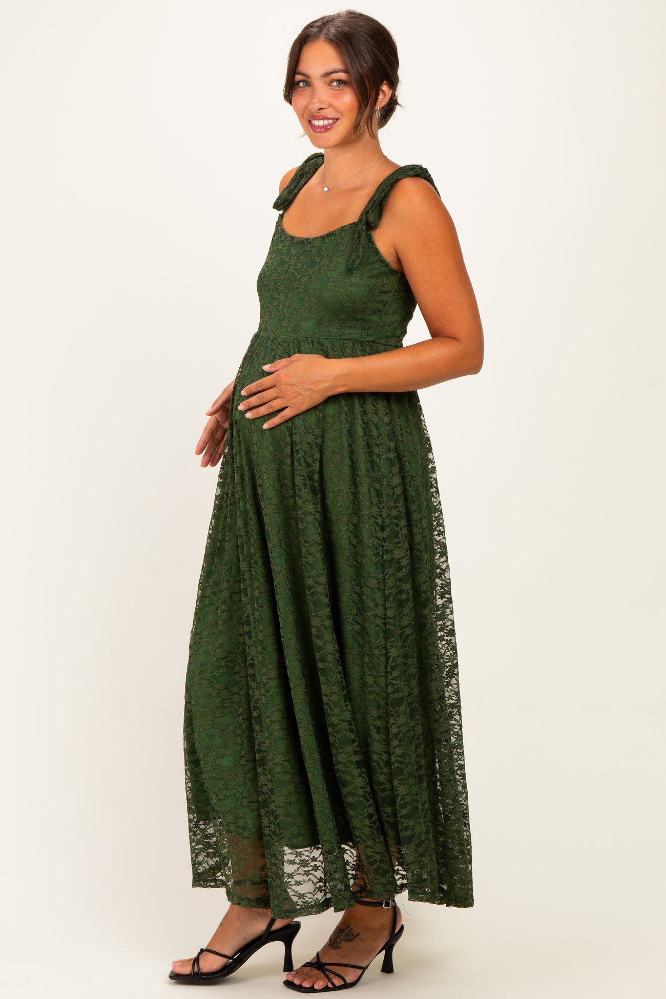 woman wearing a dark green lace maternity dress with bow straps and holding her baby bump