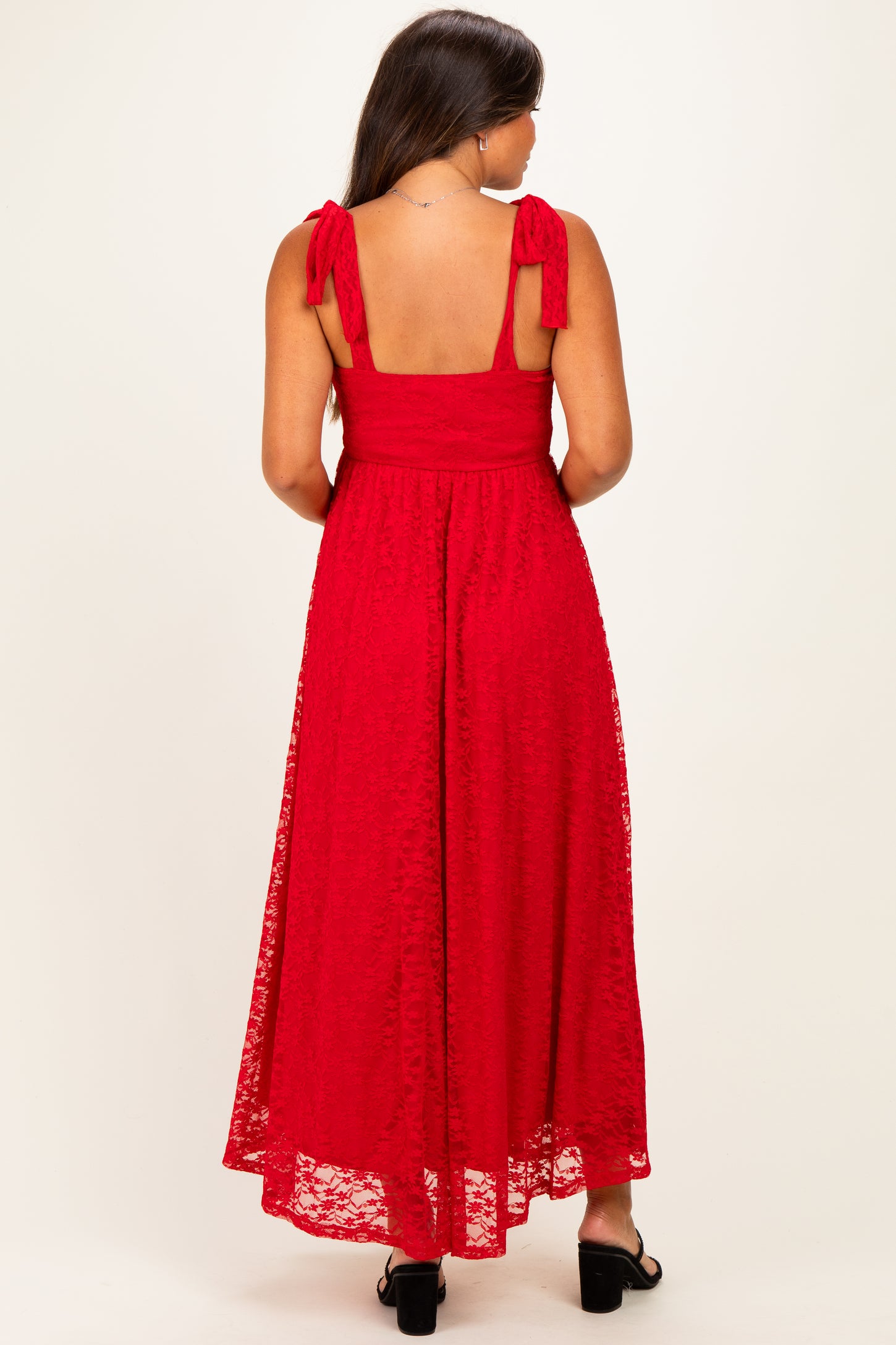 woman wearing a red lace maternity maxi dress with tie shoulder straps, showing a baby bump from the back