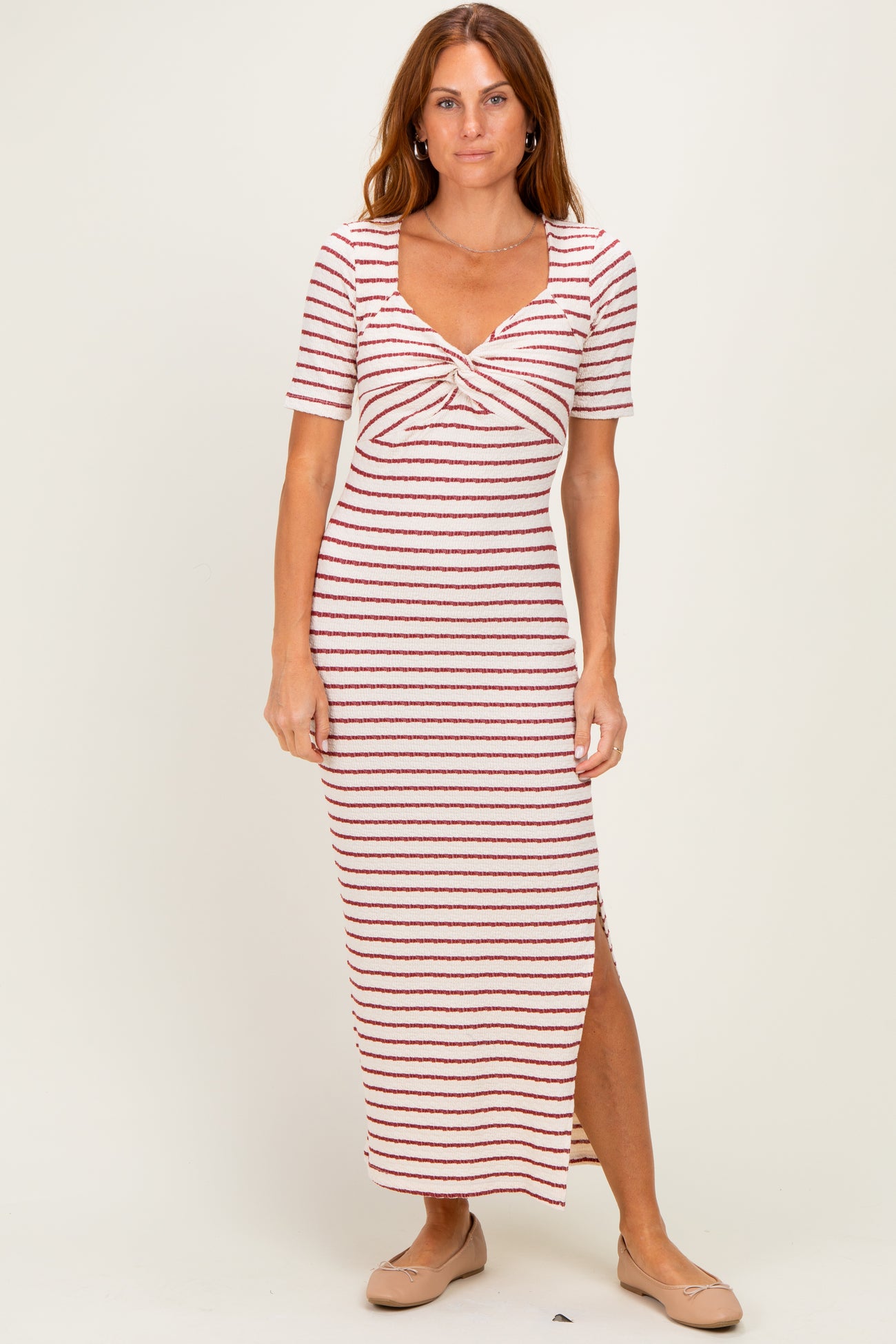 woman wearing a striped midi dress with a twisted front detail and side slit, standing on a neutral background