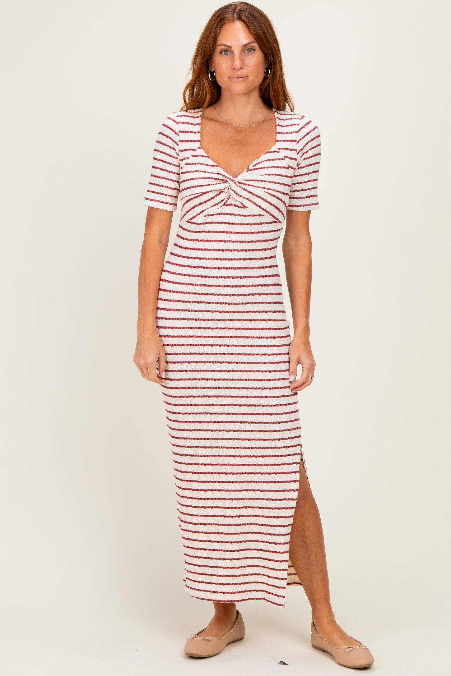 woman wearing a striped midi dress with a twisted front detail and side slit, standing on a neutral background