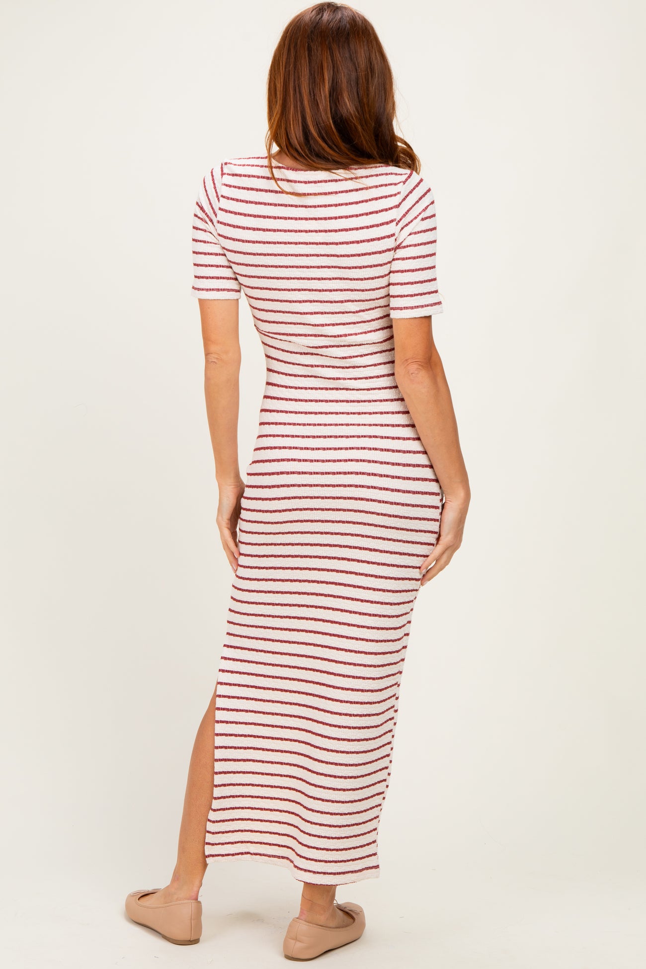 woman wearing a striped maxi dress with short sleeves and a side slit, standing with her back to the camera