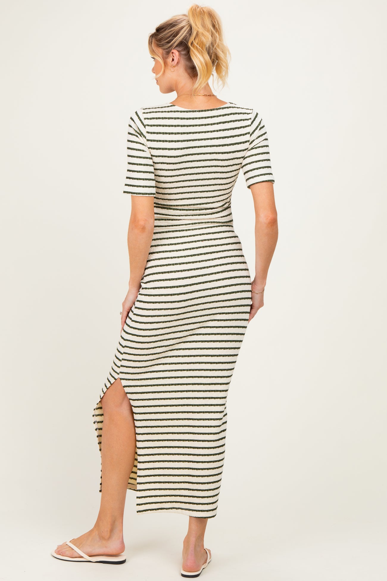 woman wearing a striped maternity maxi dress with short sleeves and a side slit, showing a baby bump from behind