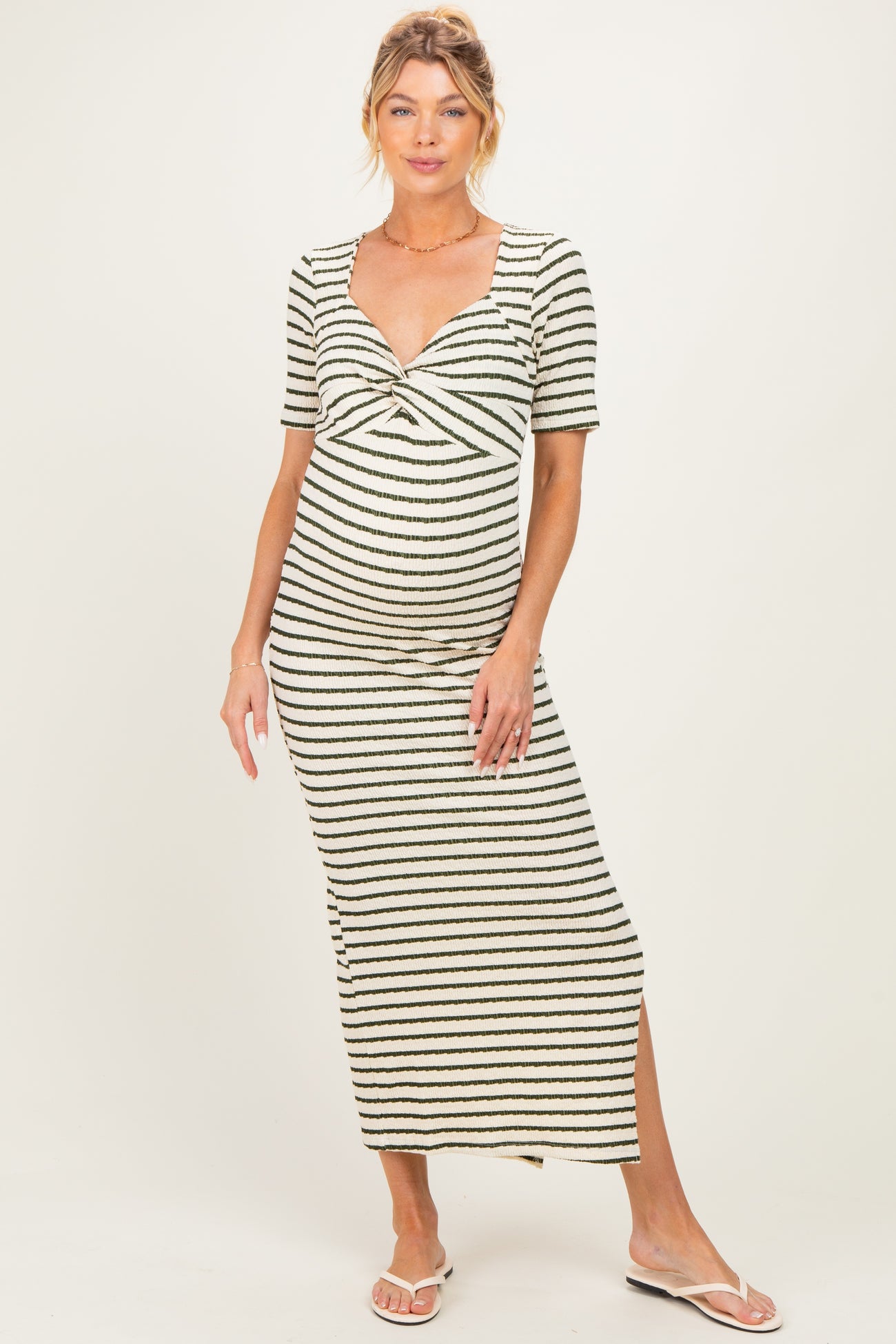woman wearing a striped maternity maxi dress with a twisted front and a side slit, highlighting her baby bump