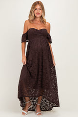 woman wearing a chocolate brown off-the-shoulder maternity dress with lace detailing and a flowing high-low hem, showing baby bump