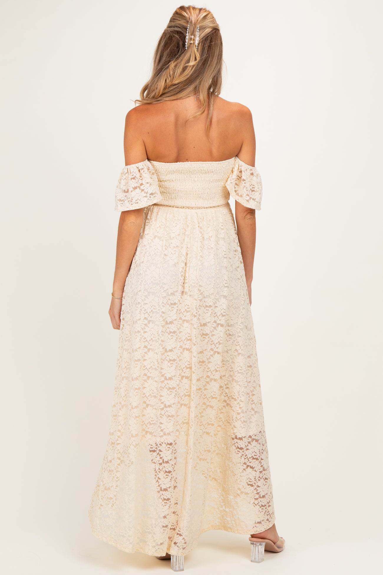woman wearing a cream off-the-shoulder lace maternity dress with a smocked bodice and flowy skirt, showing no baby bump