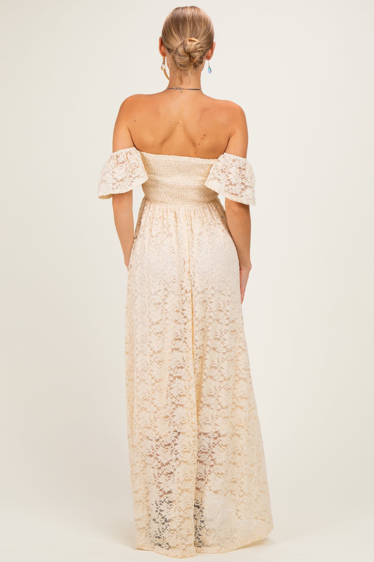 woman wearing a back view of a cream off-the-shoulder maxi dress with lace detailing and puff sleeves