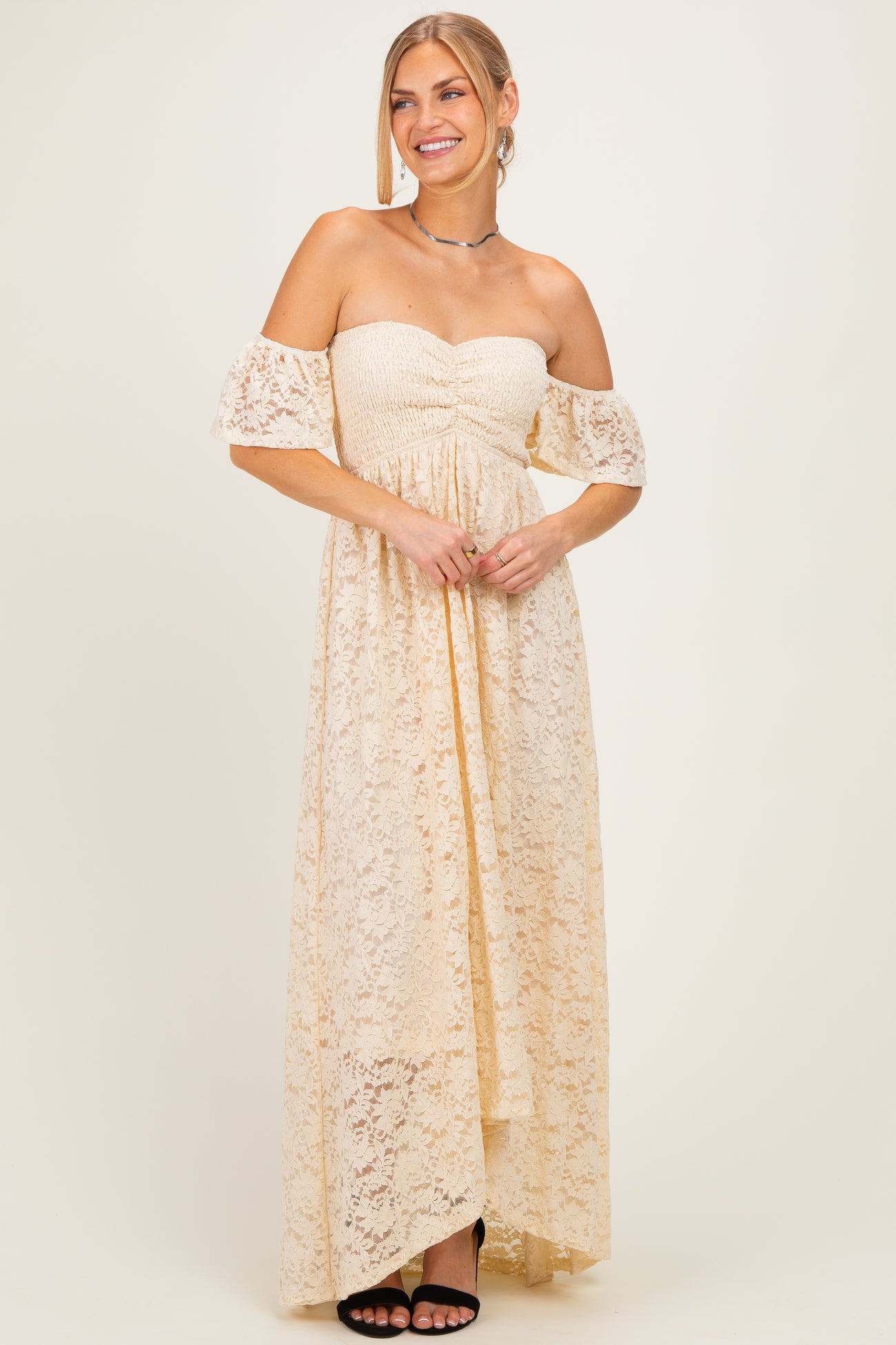 woman wearing a cream off-the-shoulder lace maxi dress with a ruched bodice and high-low hemline