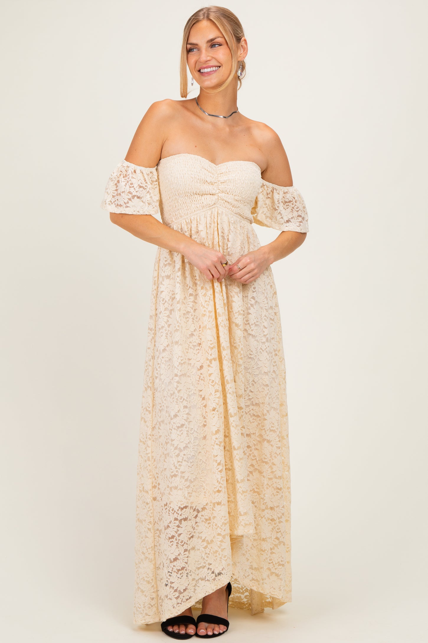 woman wearing a cream off-the-shoulder lace maxi dress with a ruched bodice and high-low hemline
