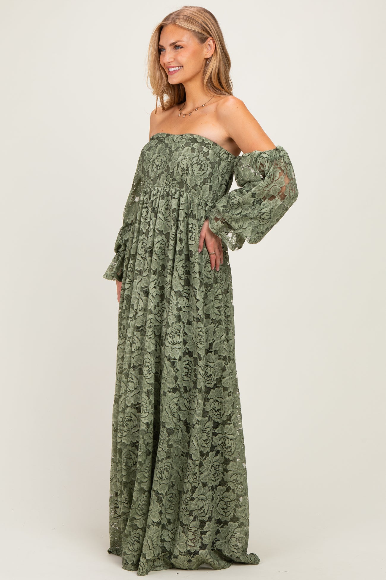 woman wearing a green off-the-shoulder maxi dress with long, sheer sleeves and floral lace detailing