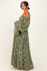 woman wearing a green lace off-the-shoulder maternity maxi dress and gently cradling her baby bump