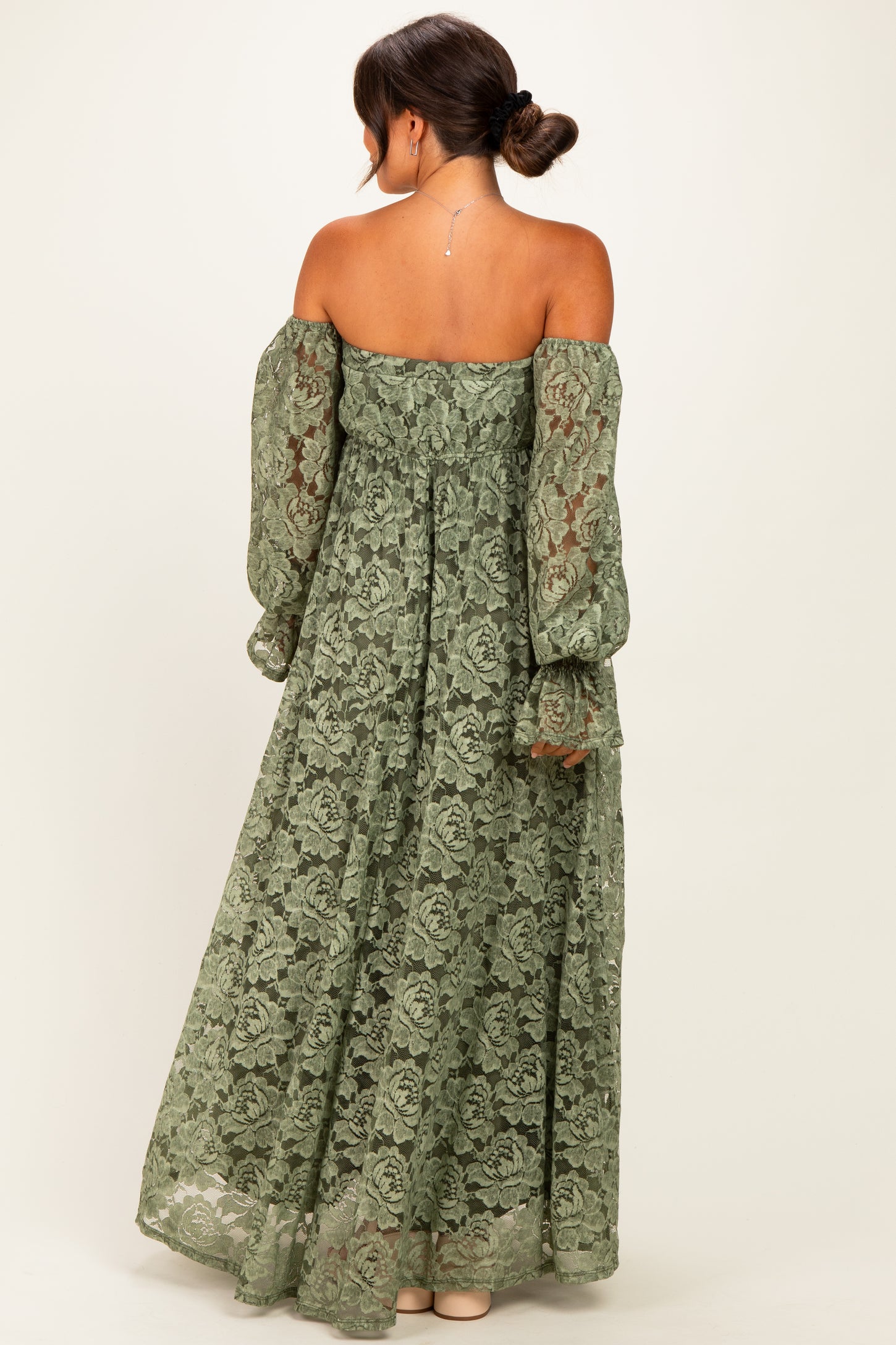 woman wearing a green lace off-the-shoulder maternity dress with long puff sleeves and a flowy silhouette