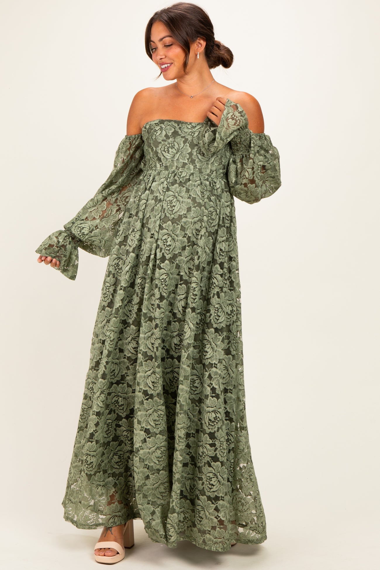 woman wearing a green lace off-shoulder maternity dress with long sleeves and a flowy skirt
