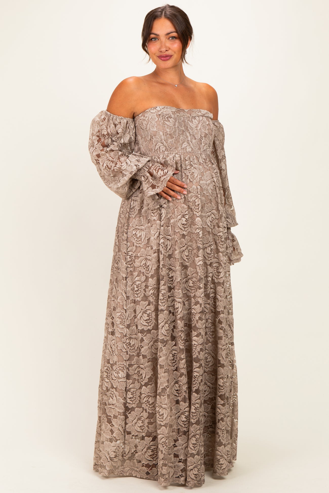 woman wearing a beige off-the-shoulder lace maternity dress with long puff sleeves and a visible baby bump