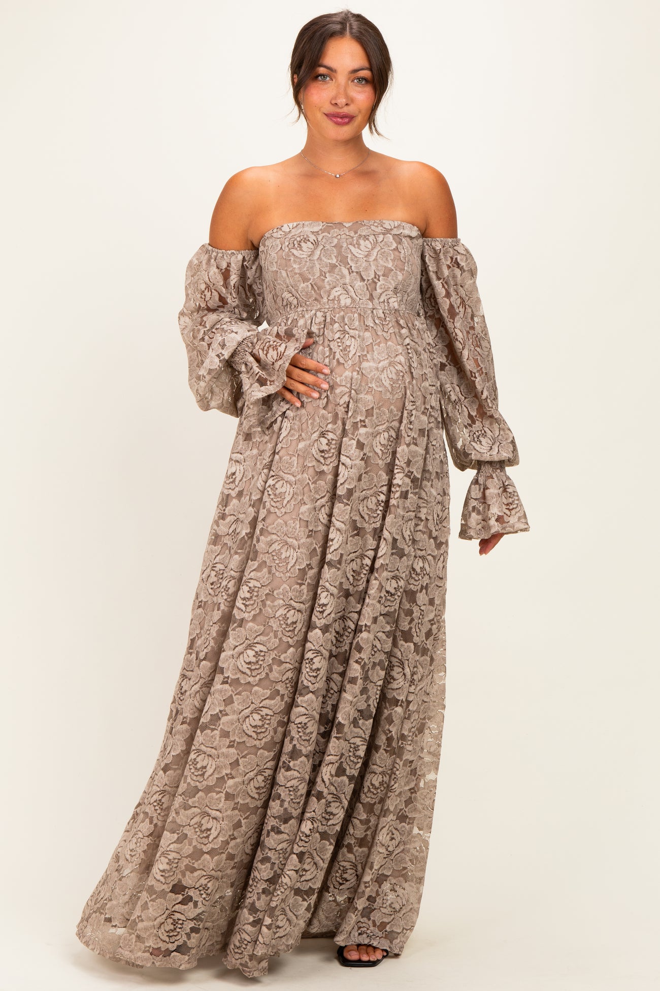 woman wearing a brown off-shoulder maternity dress with long puff sleeves and a flowing skirt, holding her baby bump