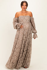 woman wearing a brown off-shoulder maternity dress with long puff sleeves and a flowing skirt, holding her baby bump