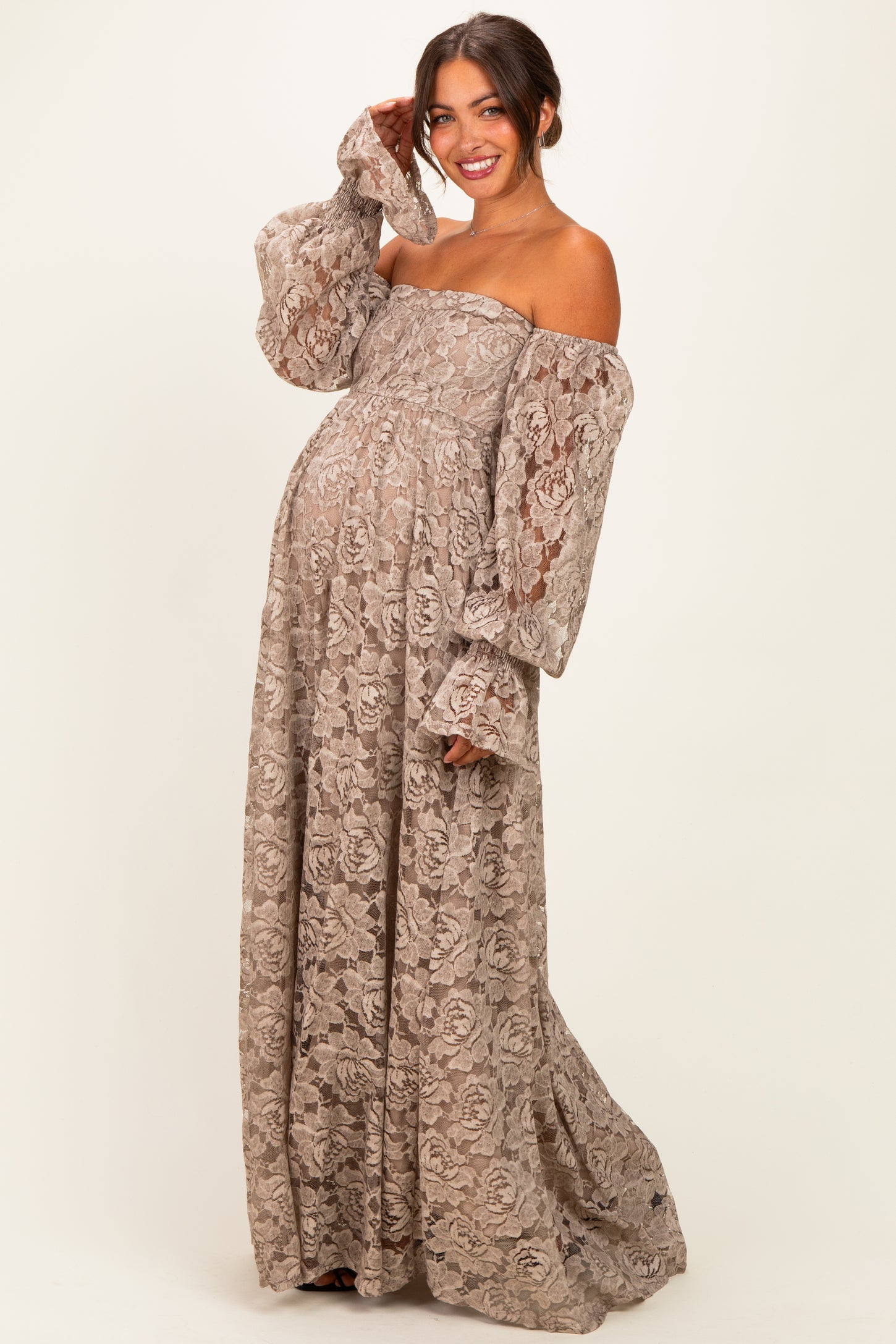 woman wearing a beige lace off-the-shoulder maternity gown with bell sleeves and a visible baby bump