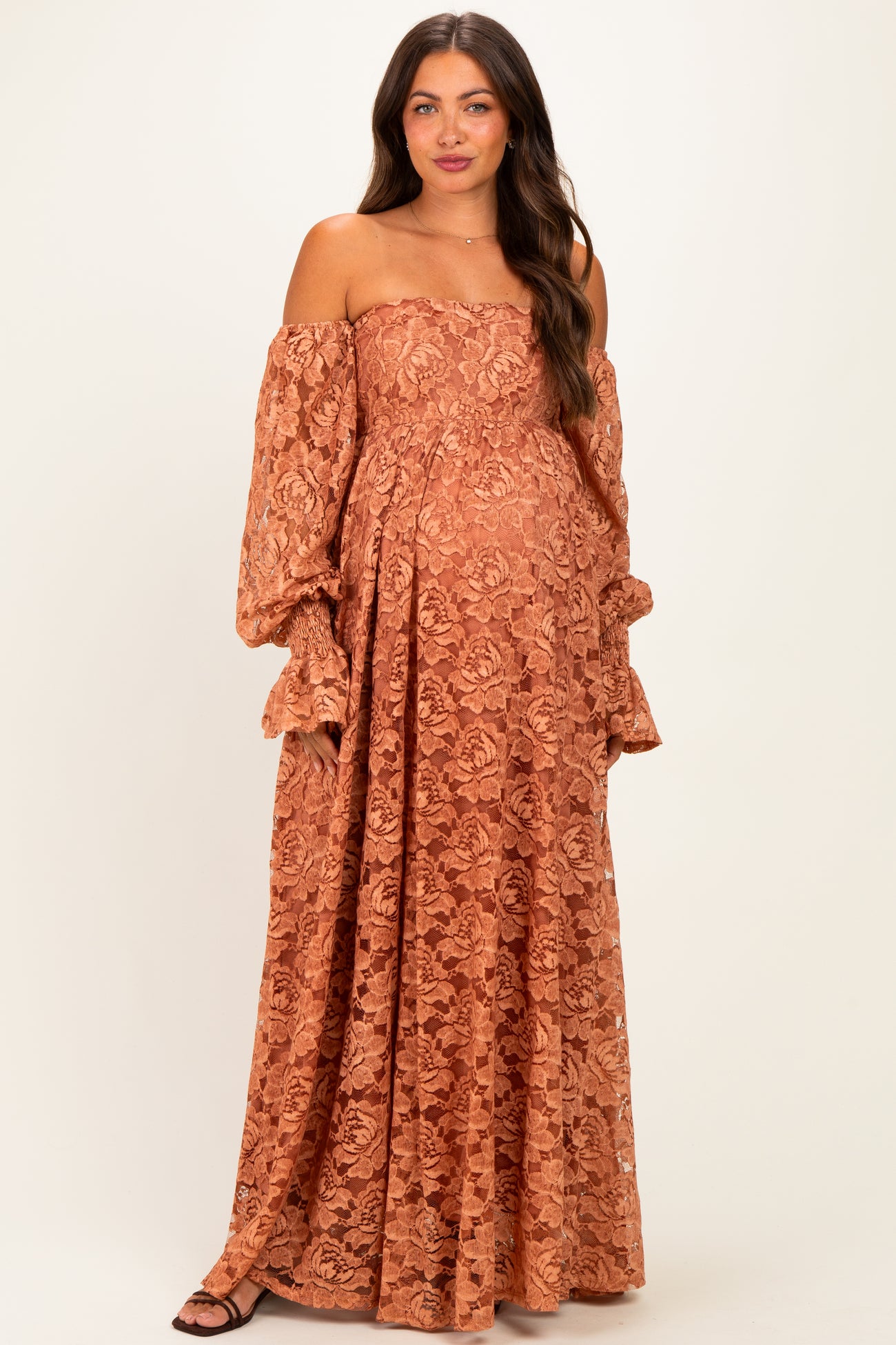 woman wearing a rust off-the-shoulder lace maternity gown with flowing sleeves and a visible baby bump