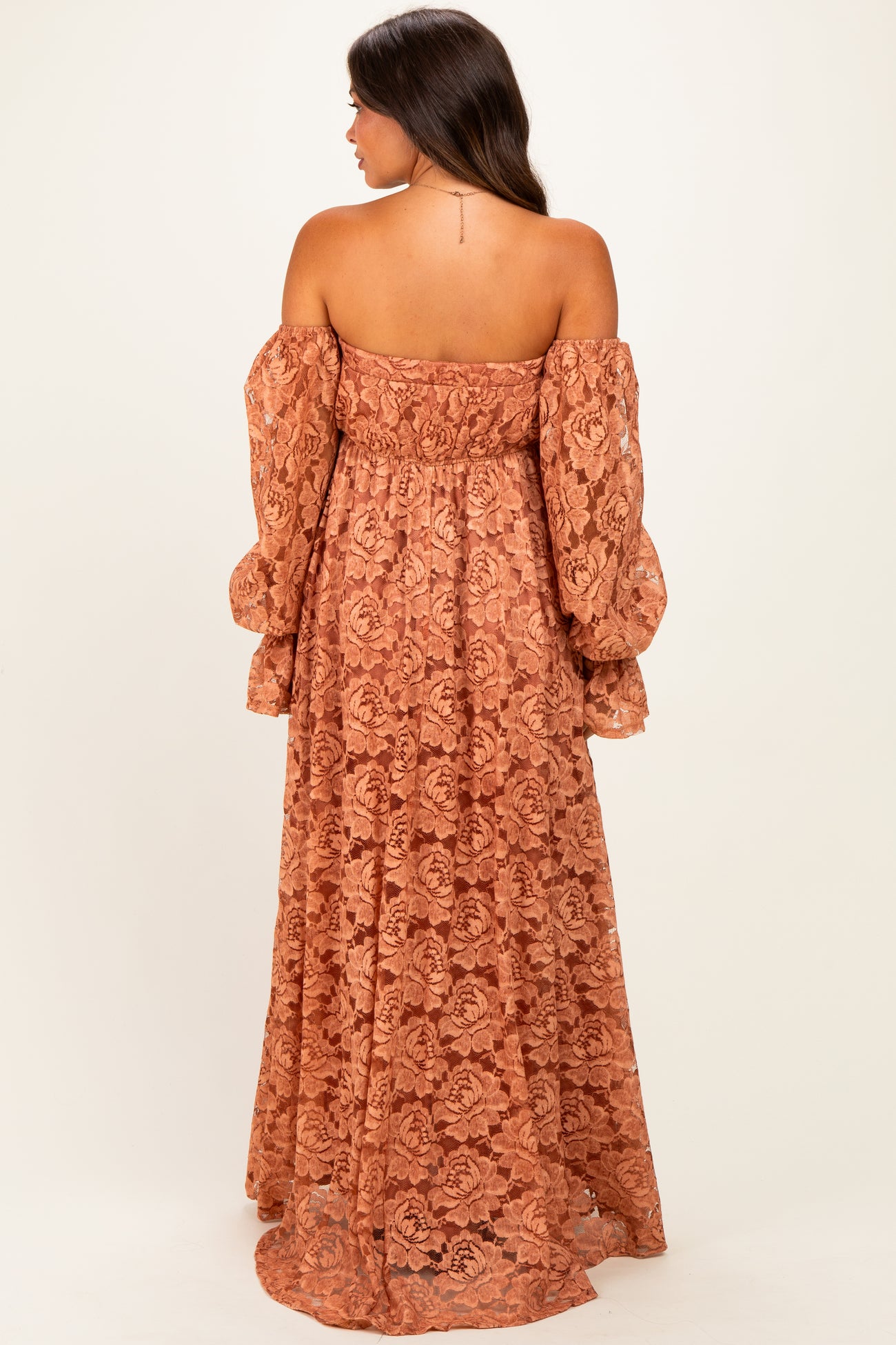 woman wearing a rust-colored off-the-shoulder lace maternity maxi dress with long puff sleeves