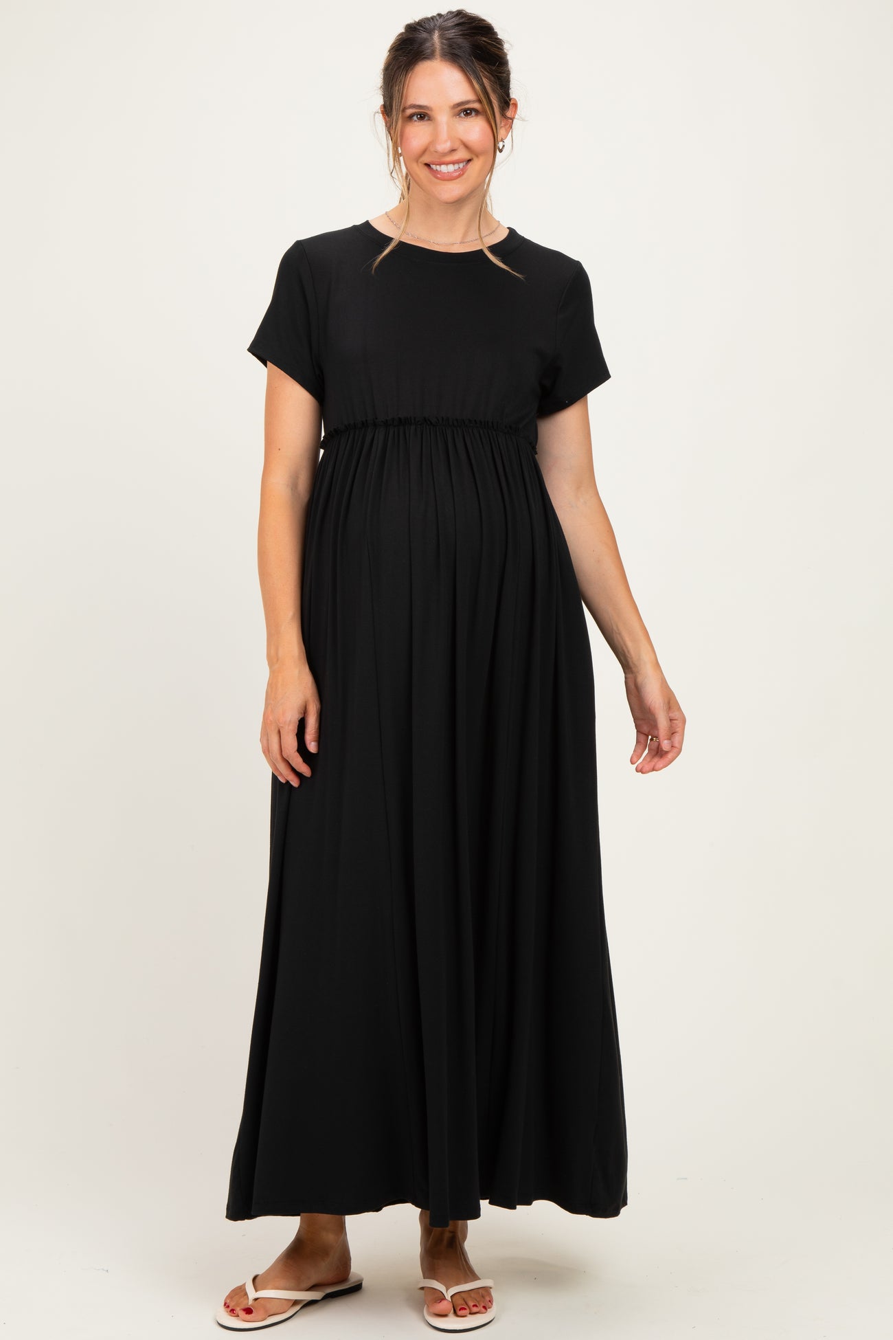 woman wearing a black short sleeve maternity maxi dress with a fitted bodice and flowy skirt, showcasing her baby bump