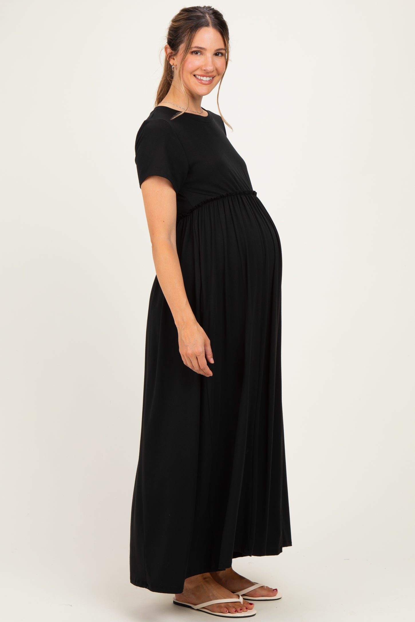 woman wearing a black short sleeve maternity maxi dress with a cinched waist and a visible baby bump