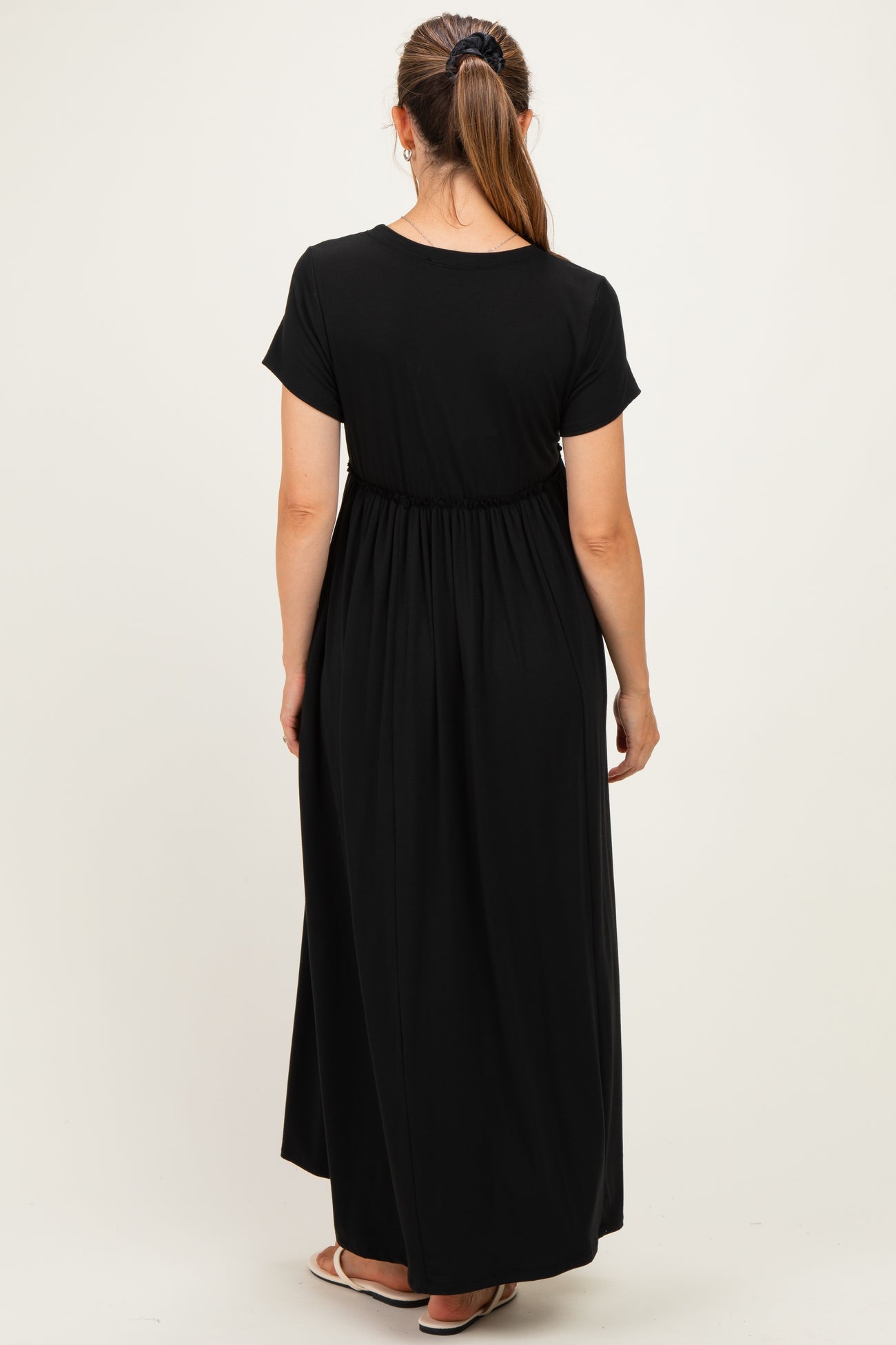 woman wearing a black short sleeve maternity maxi dress, showing a comfortable elastic waistband and flowing silhouette from the back