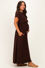 woman wearing a brown maternity maxi dress with an empire waist and pockets, showing her baby bump
