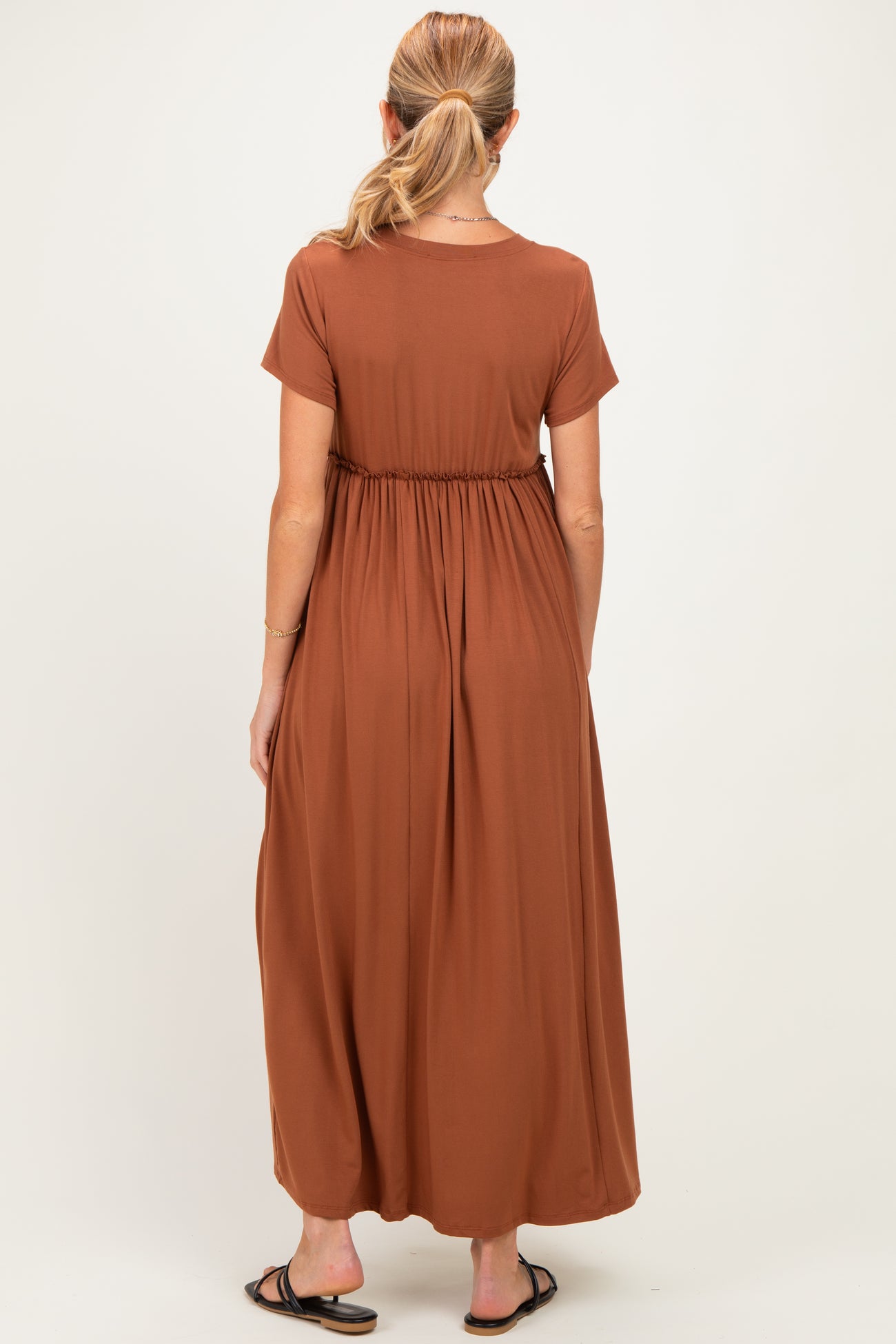 woman wearing a rust colored maternity maxi dress with short sleeves and an elastic waist, seen from the back