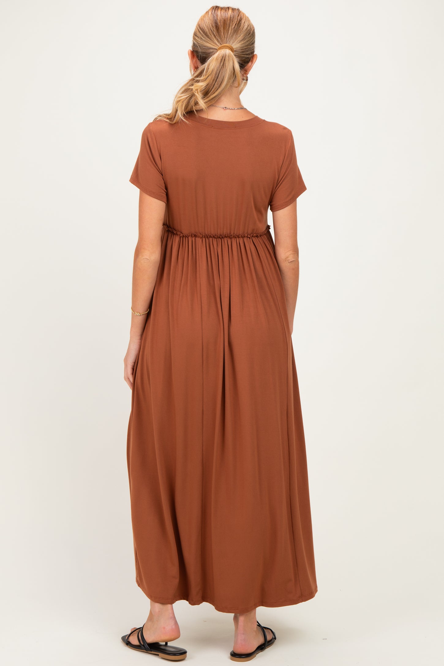 woman wearing a rust colored maternity maxi dress with short sleeves and an elastic waist, seen from the back