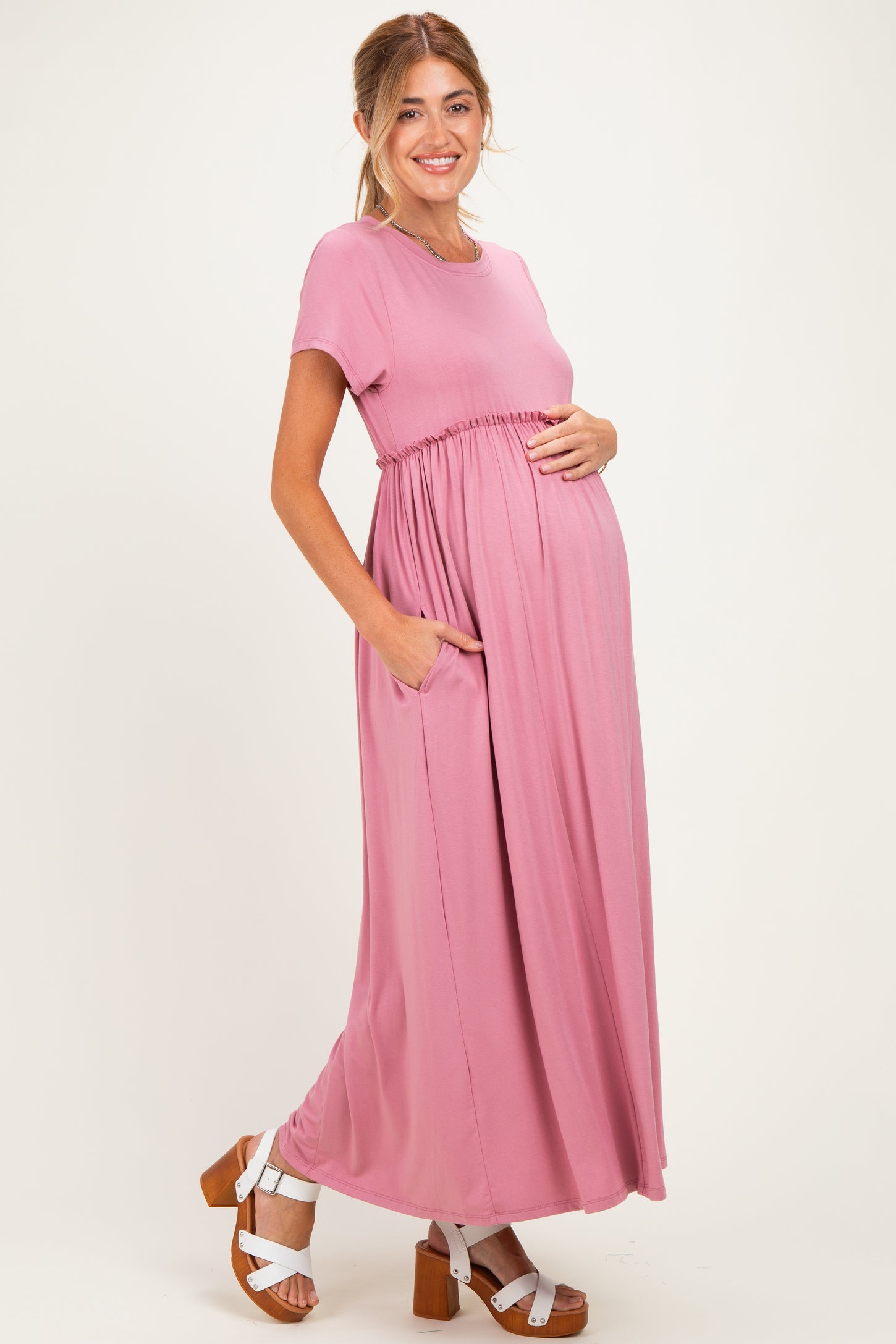 woman wearing a pink maternity maxi dress with short sleeves and pockets, showcasing her baby bump