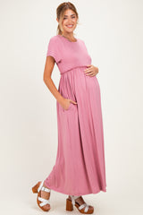 woman wearing a pink maternity maxi dress with short sleeves and pockets, showcasing her baby bump