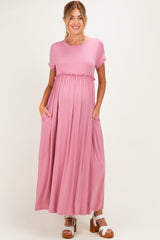 woman wearing a pink short sleeve maternity maxi dress with an elastic waist and pockets, showcasing her baby bump