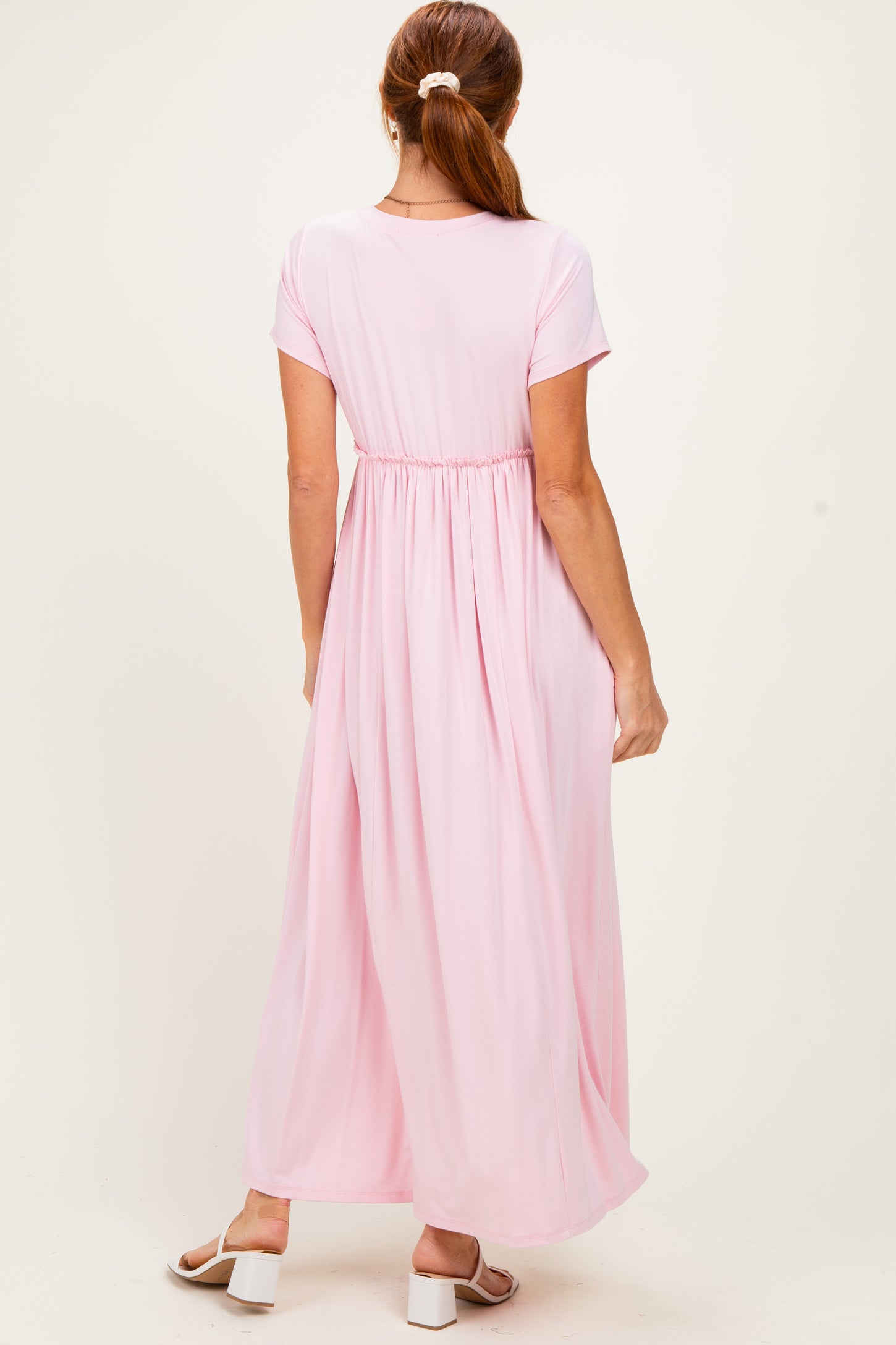 woman wearing a pastel pink short sleeve maxi dress with a cinched waist and flowing skirt, viewed from the back