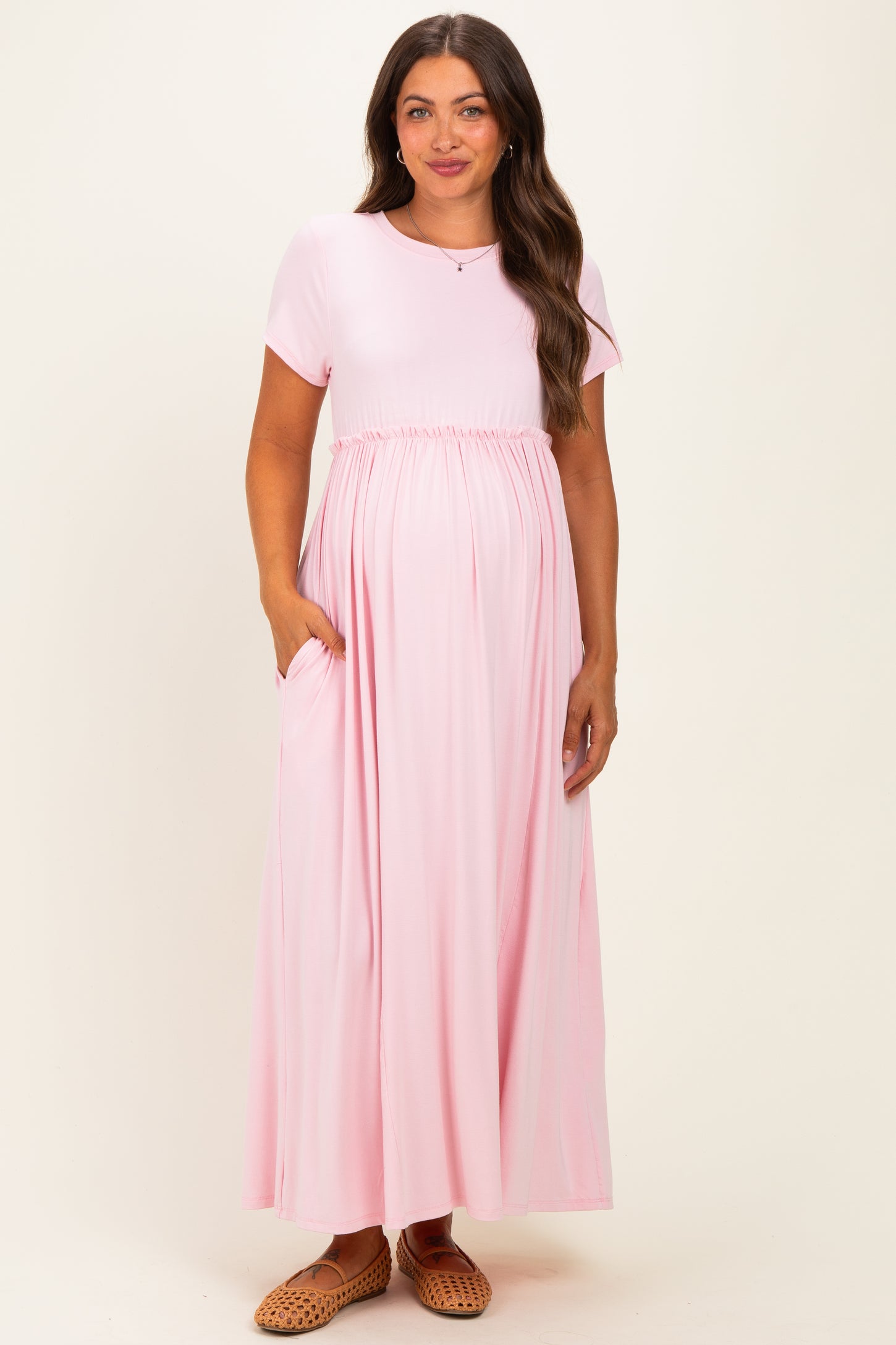 woman wearing a light pink short sleeve maternity maxi dress with an empire waist and pockets, showing her baby bump