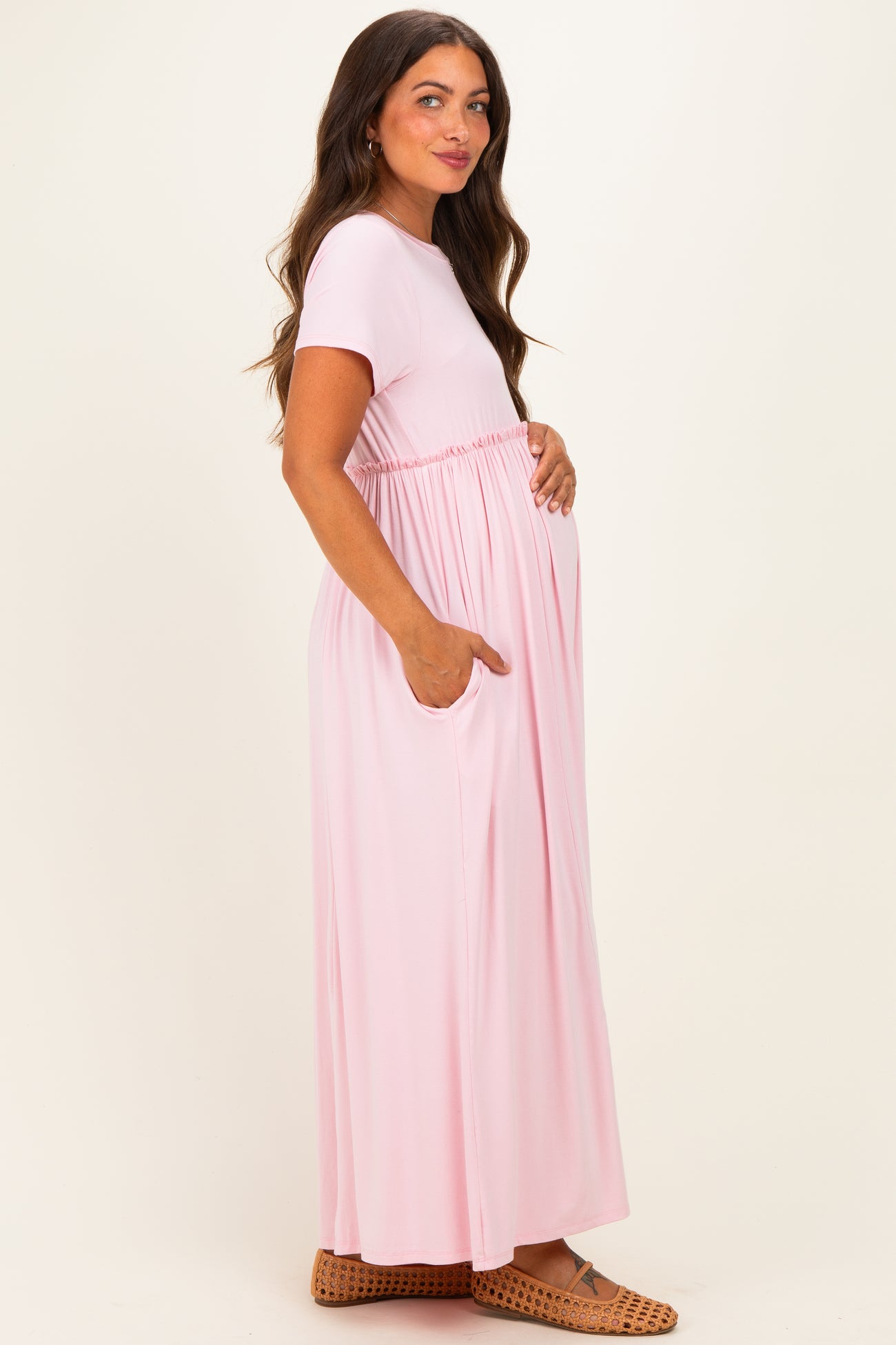 woman wearing a light pink maternity maxi dress with an elastic waist and pockets, highlighting her baby bump