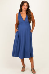 woman wearing a blue maternity dress with a deep v-neck and pockets, showcasing her baby bump