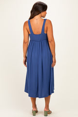 woman wearing a navy blue sleeveless maternity dress with a cinched waist and pleated skirt, showing her baby bump