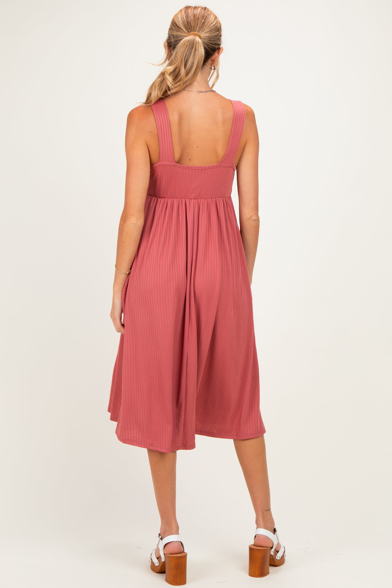 woman wearing a dusty rose maternity dress with wide straps and a flowy, pleated skirt, showcasing her baby bump