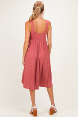 woman wearing a dusty rose maternity dress with wide straps and a flowy, pleated skirt, showcasing her baby bump