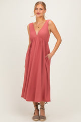 woman wearing a rust-colored sleeveless midi dress with a v-neck and pockets, standing with a slight smile
