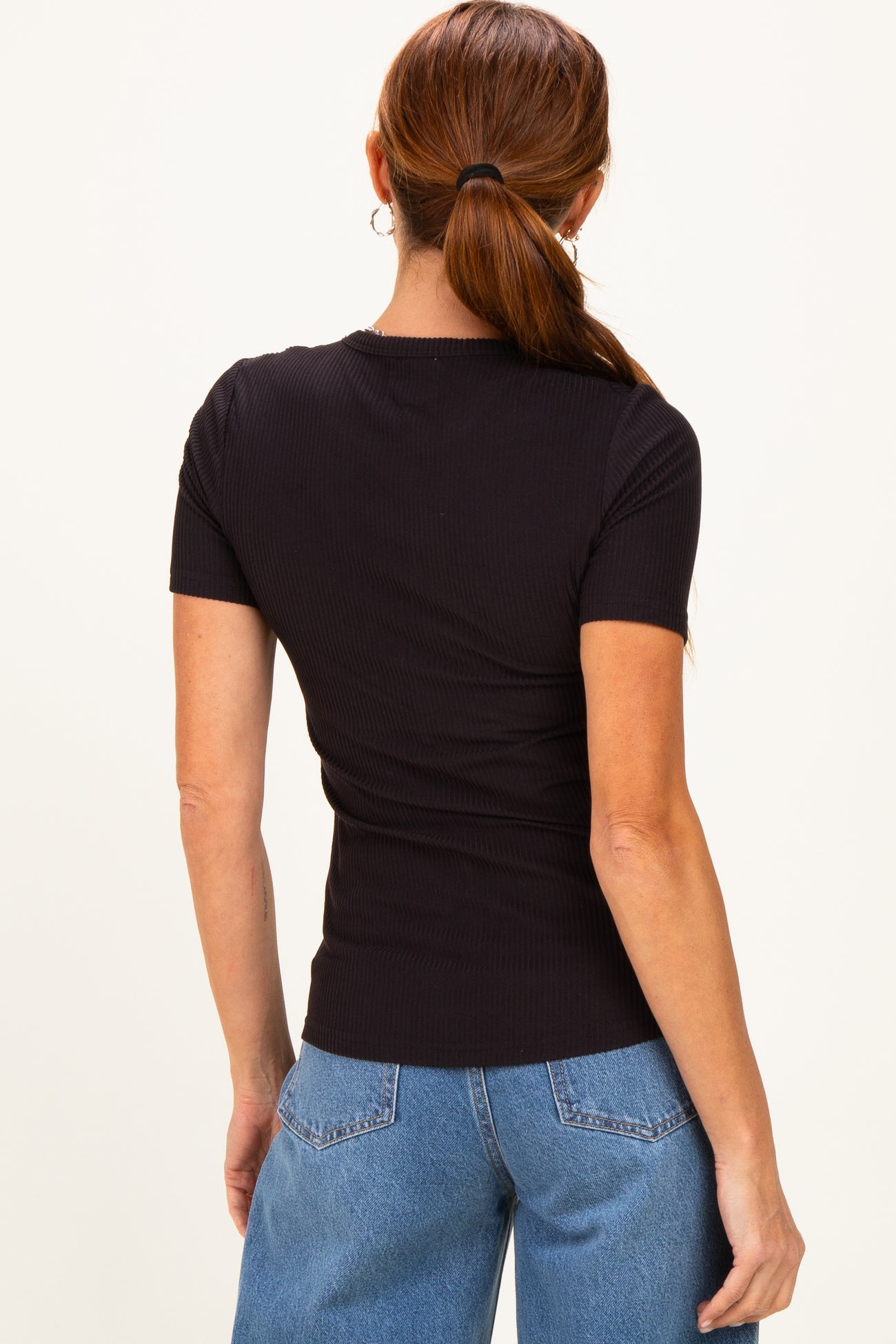woman wearing a black fitted ribbed short sleeve top with a round neckline paired with light blue jeans