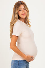woman wearing a beige ribbed maternity top and holding her baby bump while smiling