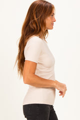 woman wearing a light beige ribbed short sleeve top, styled with black jeans, showing a side profile view