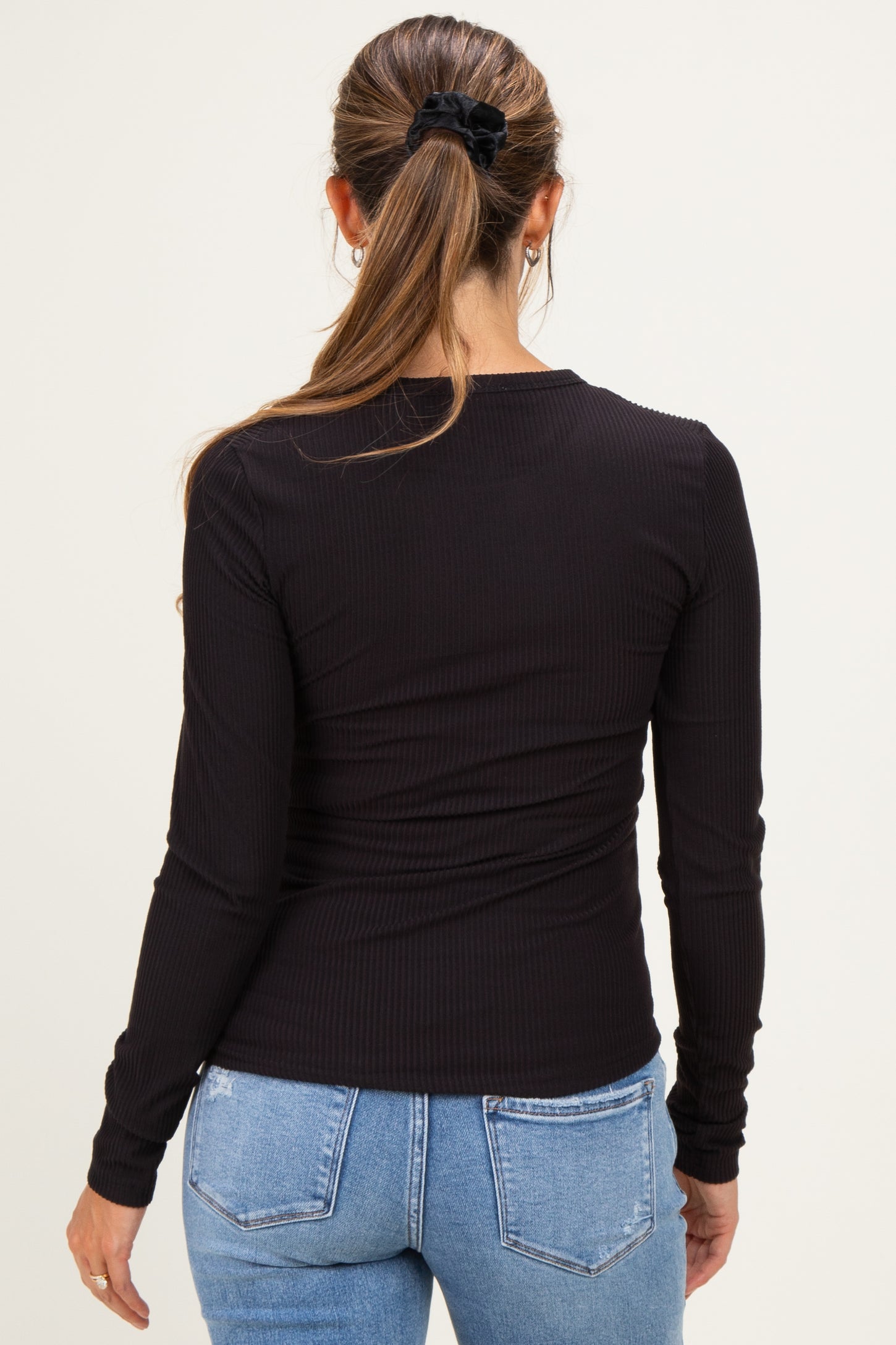 woman wearing a black long sleeve maternity top, viewed from the back with hair in a ponytail