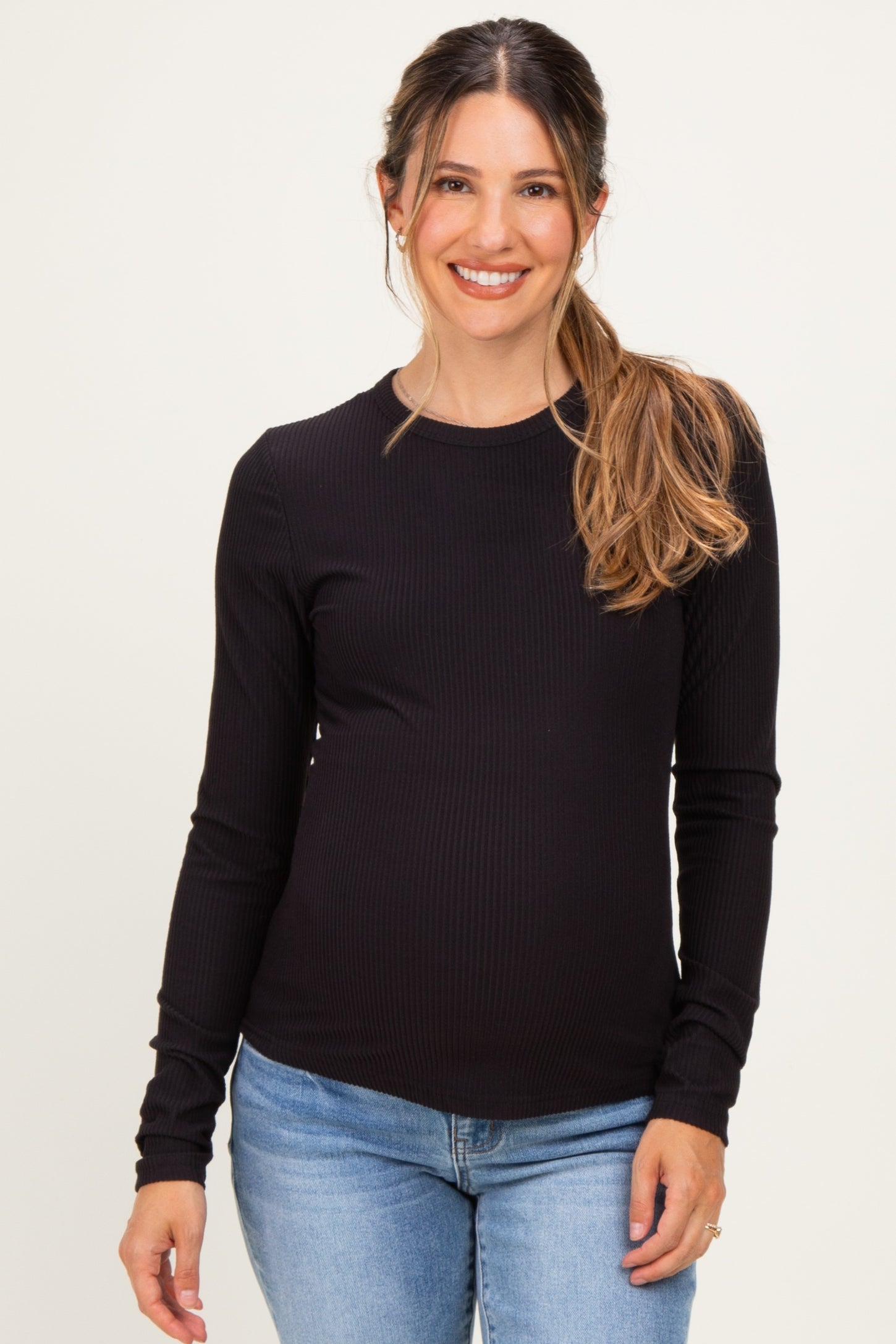 woman wearing a black long sleeve maternity top and smiling with her baby bump visible