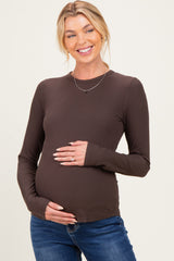 woman wearing a brown long sleeve maternity top and holding her baby bump