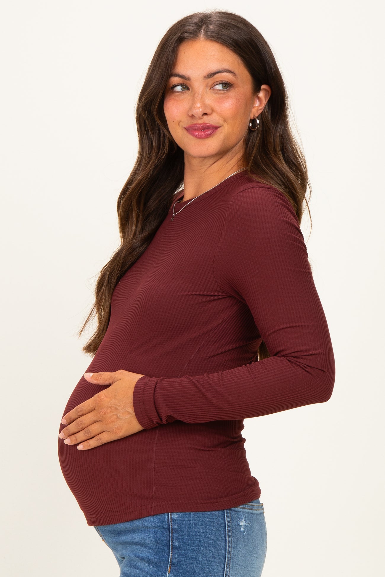 woman wearing a burgundy long sleeve maternity top and holding her baby bump