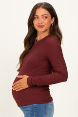 woman wearing a burgundy long sleeve maternity top and holding her baby bump