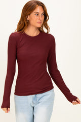 woman wearing a burgundy long sleeve ribbed top with a fitted style and round neckline, paired with light blue jeans