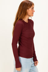 woman wearing a burgundy long sleeve ribbed top with fitted style and thumb holes, paired with light blue jeans